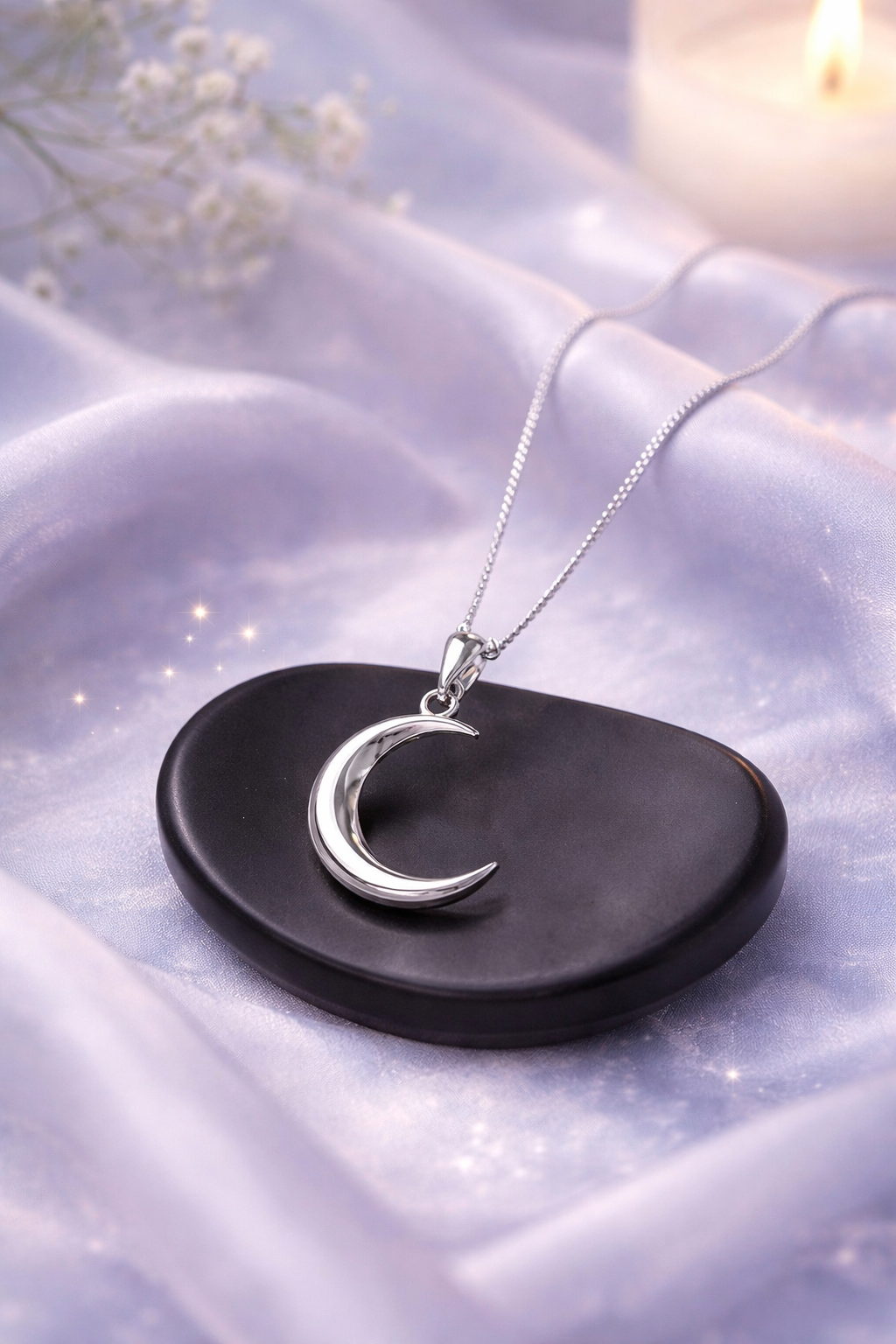 Silver moon-shaped pendant on a chain, placed on a dark stone surface with a soft background.